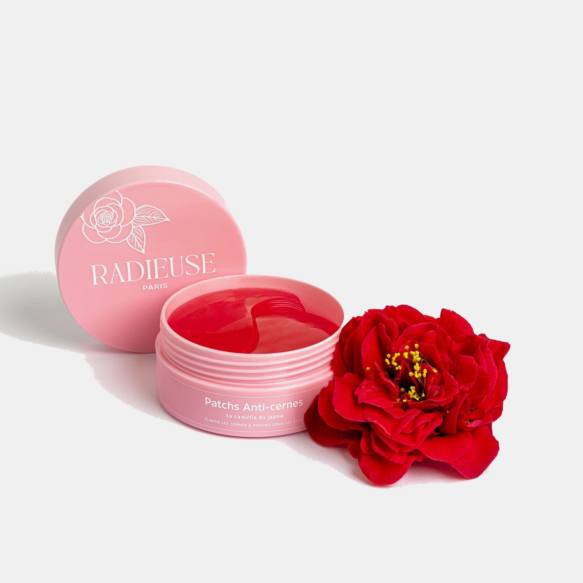 Pot rose de patchs anti-cernes Radieuse Paris ouvert, avec un patch rouge à l'intérieur, accompagné d'une fleur de camélia rouge. Patchs au Camélia Japonica, conçus pour réduire les cernes et poches sous les yeux, naturels, vegan et cruelty-free. Livraison offerte dès 40€ en France.