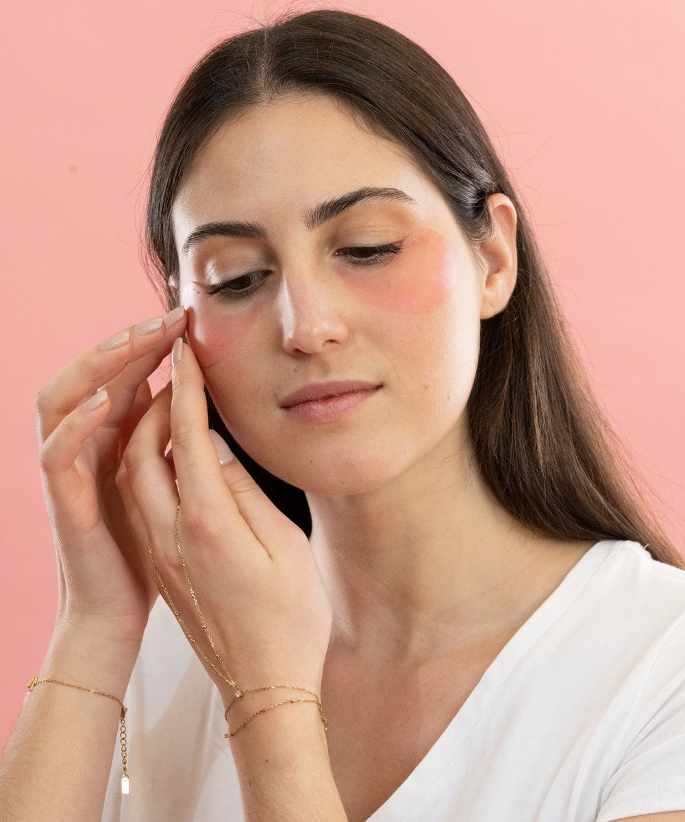 Femme appliquant les patchs anti-cernes Radieuse Paris sous ses yeux. Étape 1 : Nettoyez votre visage pour une absorption optimale. Étape 2 : Ajustez les patchs pour qu’ils couvrent bien la zone des cernes et des poches. Étape 3 : Laissez poser les patchs pendant 15 à 20 minutes pour des résultats optimaux. Étape 4 : Retirez et tapotez doucement du bout des doigts pour faire pénétrer les actifs, sans rinçage. Patchs naturels au Camélia Japonica, vegan, cruelty-free et évalués 100% sur YUKA.Livraison offerte