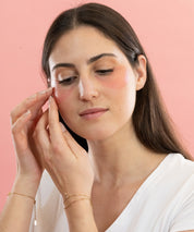 Femme appliquant les patchs anti-cernes Radieuse Paris sous ses yeux. Étape 1 : Nettoyez votre visage pour une absorption optimale. Étape 2 : Ajustez les patchs pour qu’ils couvrent bien la zone des cernes et des poches. Étape 3 : Laissez poser les patchs pendant 15 à 20 minutes pour des résultats optimaux. Étape 4 : Retirez et tapotez doucement du bout des doigts pour faire pénétrer les actifs, sans rinçage. Patchs naturels au Camélia Japonica, vegan, cruelty-free et évalués 100% sur YUKA.Livraison offerte