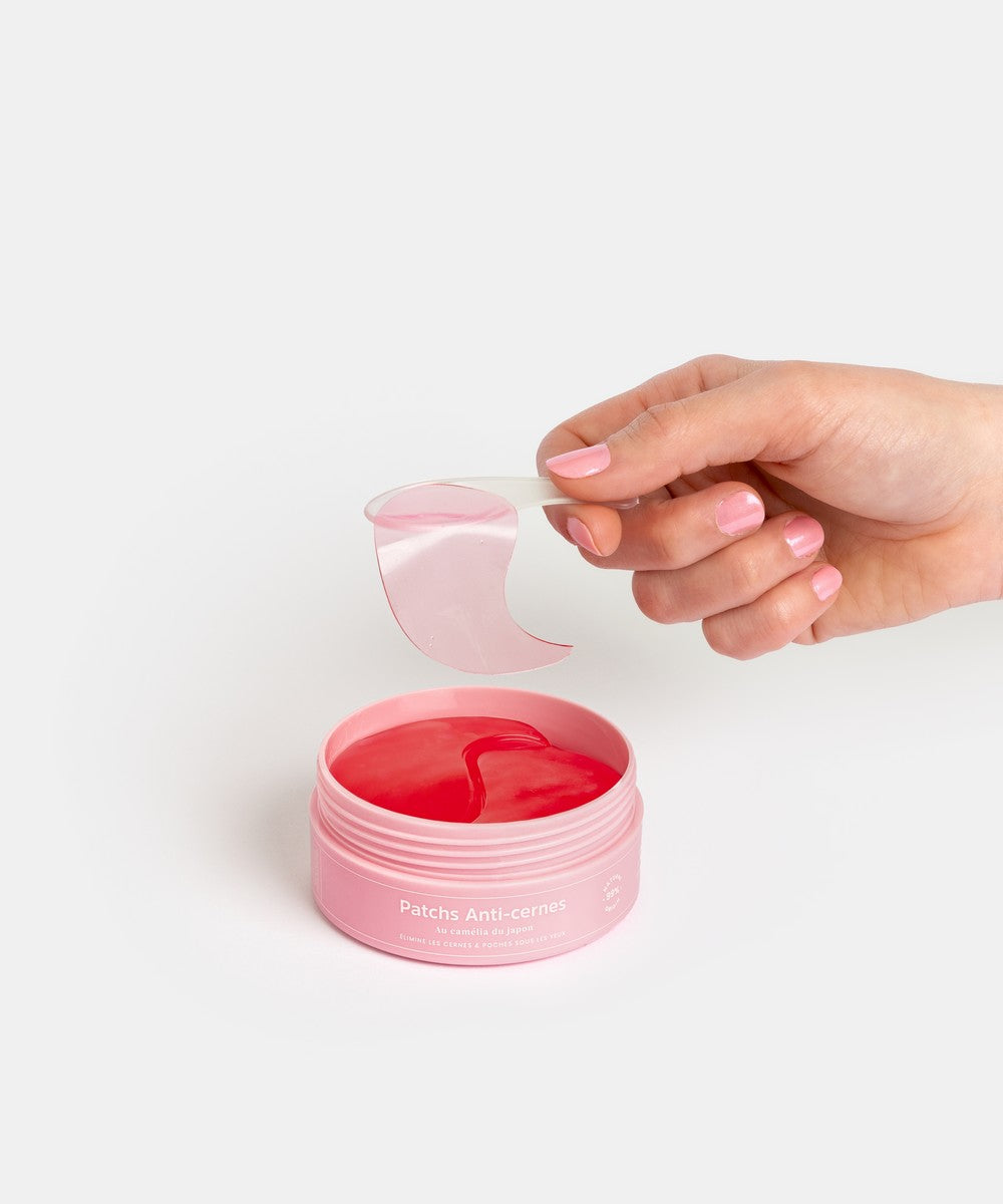 Main retirant un patch anti-cernes Radieuse Paris du pot rose, avec le produit visible à l&#39;intérieur. Patchs au Camélia Japonica, conçus pour réduire les cernes et poches sous les yeux, naturels, vegan et cruelty-free. Livraison offerte dès 40€ en France.