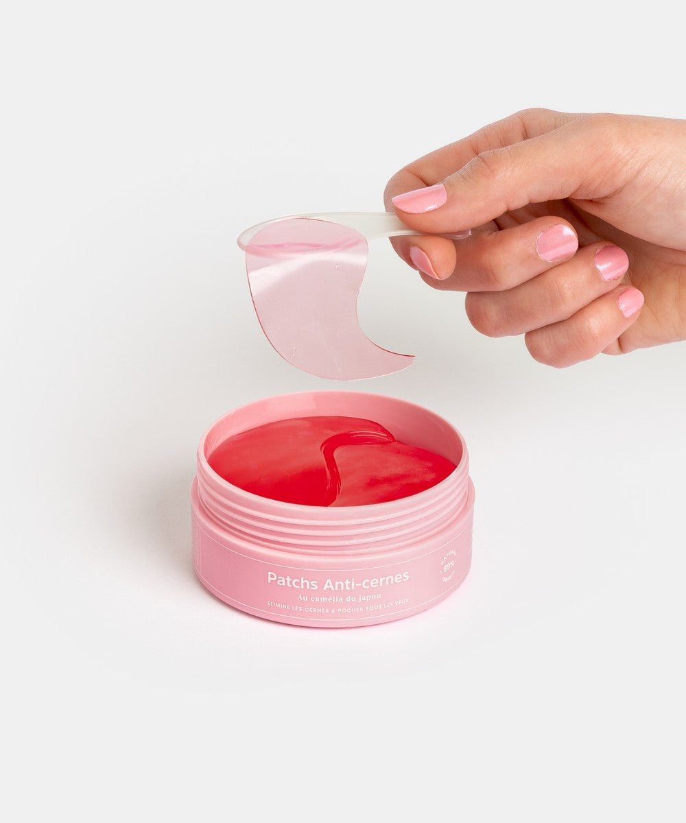 Main retirant un patch anti-cernes Radieuse Paris du pot rose, avec le produit visible à l'intérieur. Patchs au Camélia Japonica, conçus pour réduire les cernes et poches sous les yeux, naturels, vegan et cruelty-free. Livraison offerte dès 40€ en France.