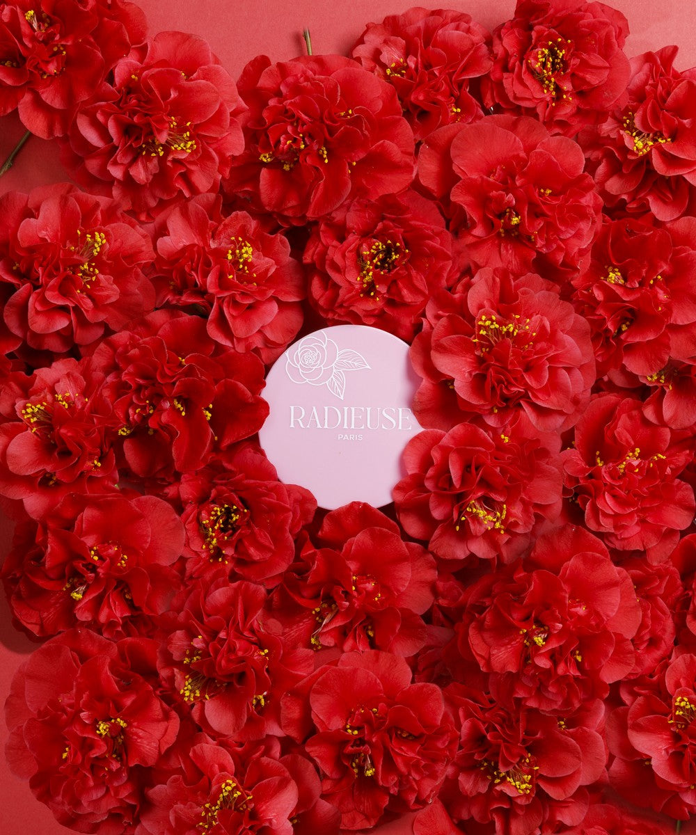 Produit cosmétique Radiéuse Paris mis en valeur par des fleurs de Camélia du Japon rouges éclatantes, symbole d'élégance et de beauté naturelle.