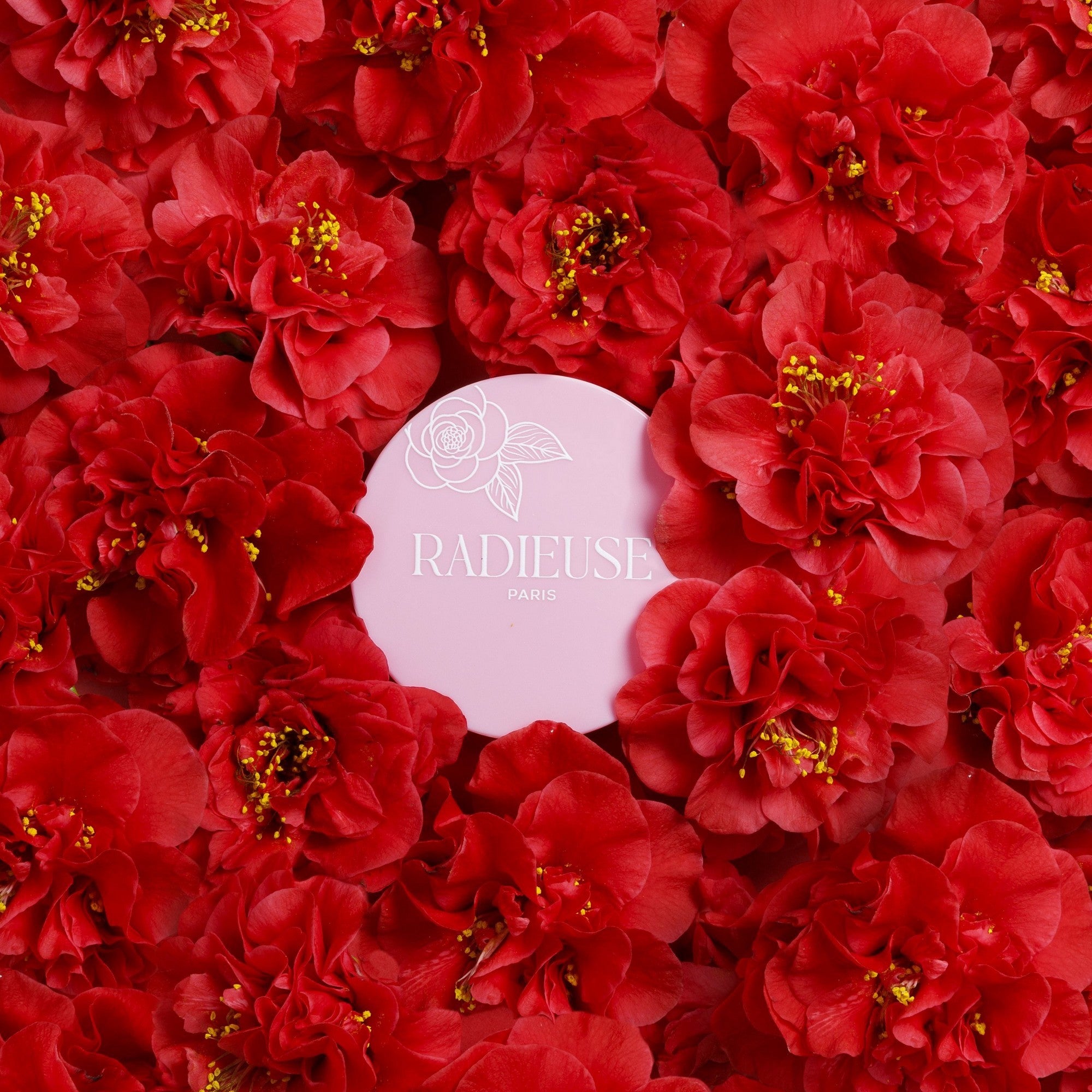 Produit cosmétique Radiéuse Paris mis en valeur par des fleurs de Camélia du Japon rouges éclatantes, symbole d'élégance et de beauté naturelle.