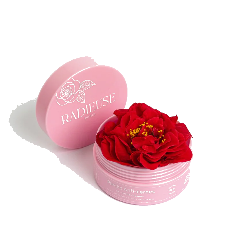 Boîte rose des patchs anti-cernes Radieuse Paris ouverte, révélant une fleur de Camélia Japonica rouge vif à l&#39;intérieur. Ce visuel met en avant l&#39;ingrédient naturel clé du produit, connu pour ses propriétés hydratantes et apaisantes pour le contour des yeux.
L&#39;huile de camélia ( tsubaki en japonais ) l&#39;ingrédient phare de notre formule, riche en oméga-6 et 9, renforce la barrière cutanée et prévient la déshydratation. Grâce à elle, nos patchs offrent un effet &quot;Glass-skin&quot; et anti-âge immédiat.